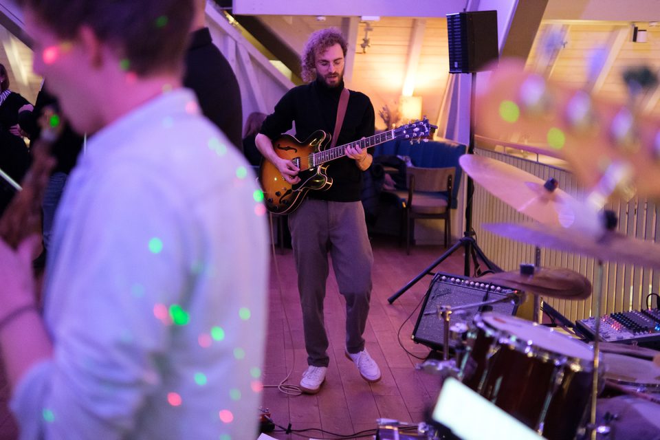 Portrait des Gitarristen einer Band mit weiteren Instrumenten in der Unschärfe