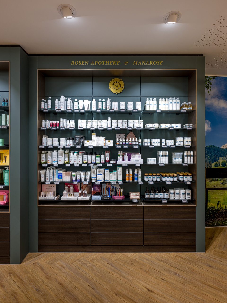 Regalwand mit goldenem Schriftzug „Rosen Apotheke & Manarose" und dem Rosenemblem über den Pflegeprodukten