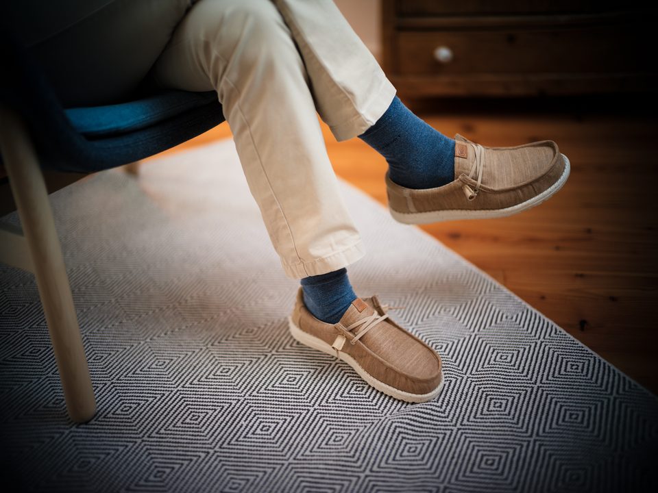 Verschränkte Beine mit heller Hose, blauen Socken und ockerfarbenen Schuhen im Sessel der Praxis