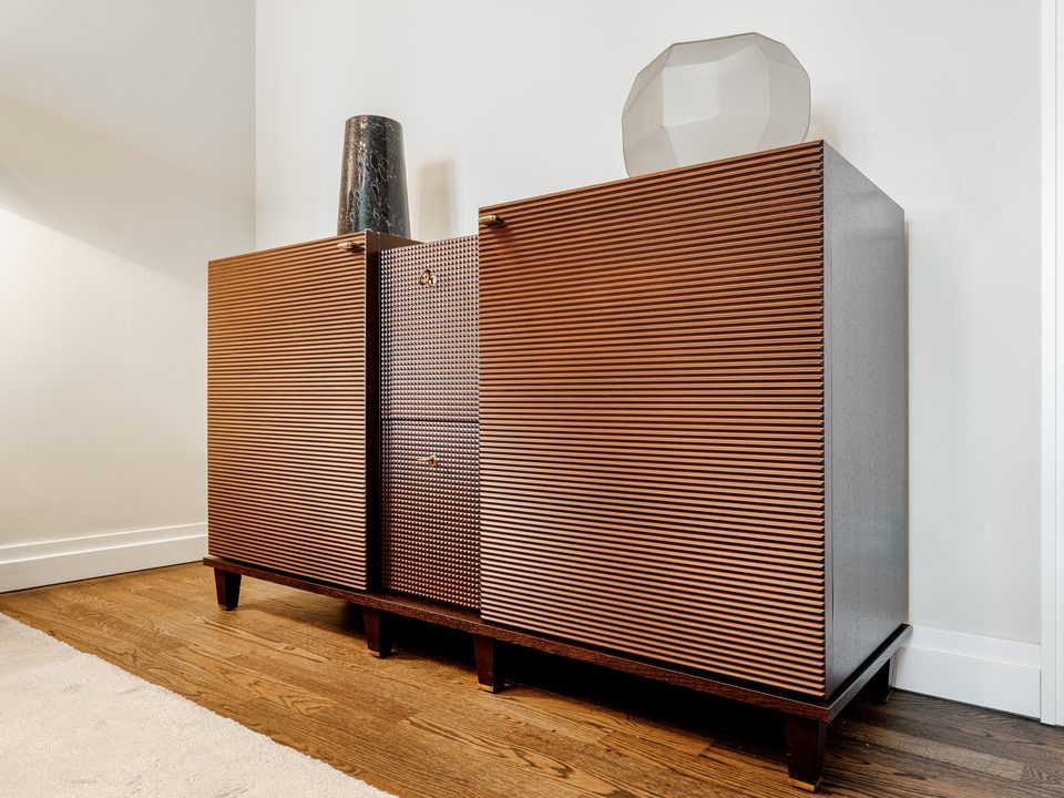 Sideboard mit geriffelten Türen und Vasen an einer weißen Wand