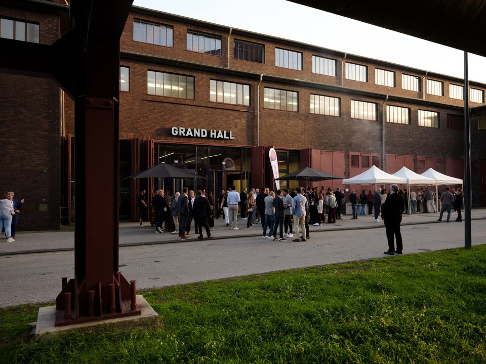 Gäste vor dem Klinkerbau der Grand Hall Zollverein mit weißen Pavillons im Sonnenschein, vorn ein rostiger Stahlträger