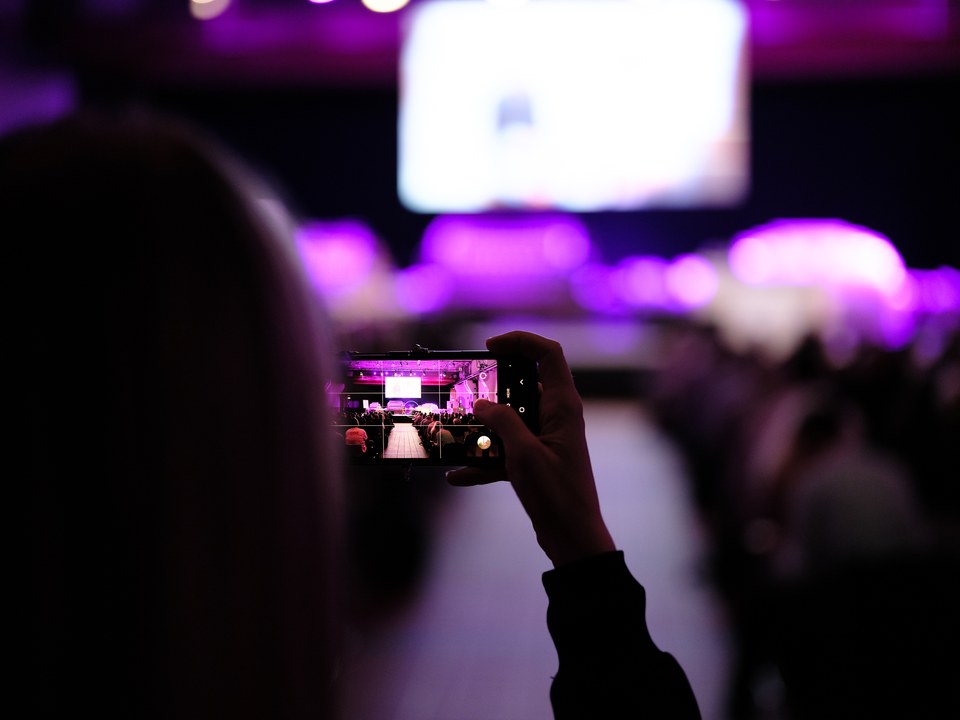Eine Zuschauerin filmt mit dem Smartphone die violett beleuchtete Bühne
