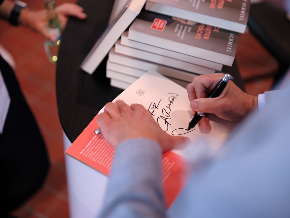 Eine Hand signiert ein Buch, daneben ein Stapel weiterer Exemplare