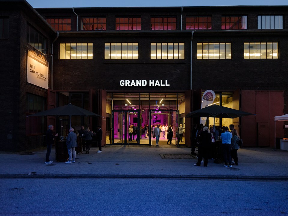 Die beleuchtete Fassade der Grand Hall am Abend, Gäste vor dem Eingang