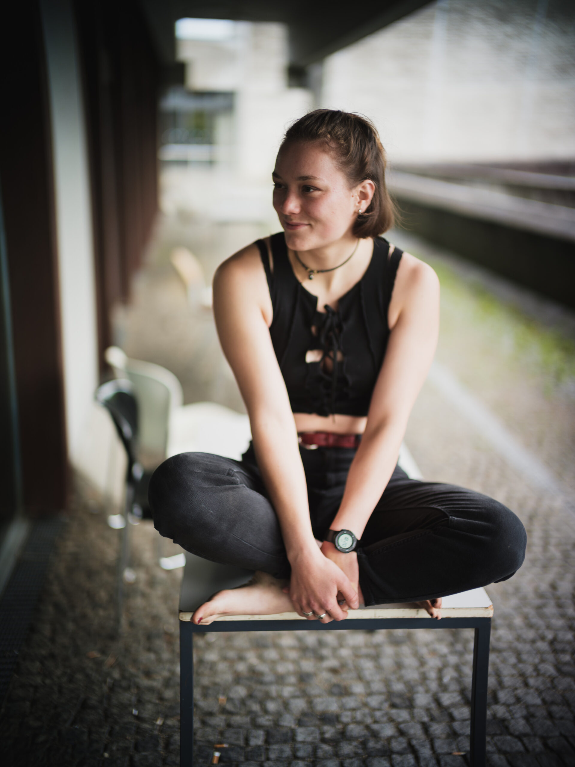 Portraitfoto einer jungen Frau auf dem Gelände der Universität Regensburg, lächelnd auf einem Tisch sitzend, Blick aus dem Bild heraus.