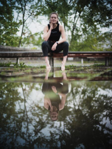 Portraitfoto einer jungen Frau auf dem Gelände der Universität Regensburg mit Spiegelung auf einer Wasserfläche.
