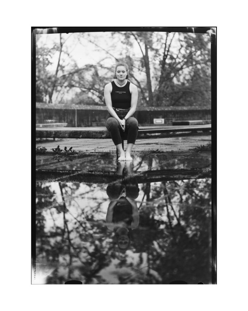 Portrait der Studentin Ida mit Spiegelung in einer Wasseransammlung auf dem Gelände der Regensburger Universität mit einer Großbildkamera auf Negativfilm