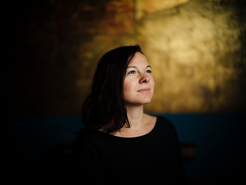 Frau mit dunklen, mittellangen Haaren professionell fotografiert in der Vinyl Bar Regensburg mit sehr schmalem Schärfebereich und goldenem Hintergrund