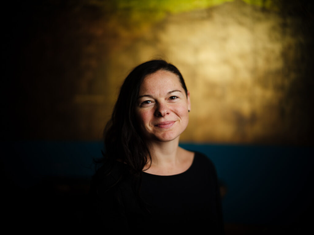 Frau mit dunklen, mittellangen Haaren professionell fotografiert in der Vinyl Bar Regensburg mit sehr schmalem Schärfebereich und goldenem Hintergrund