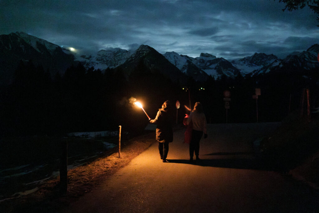 Menschen auf einer Fackelwanderung vor dem Hintergrund der nachtschwarzen Allgäuer Alpen