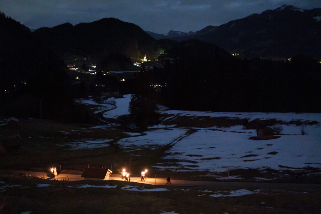 Menschen auf einer Fackelwanderung vor dem Hintergrund der nachtschwarzen Allgäuer Alpen