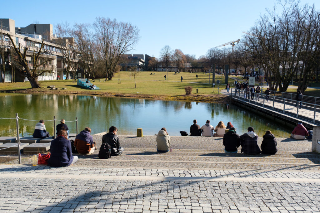 Einige Besucher der DPG-Frühjarstagung sitzen auf den Stufen am kleinen See der Universität Regensburg