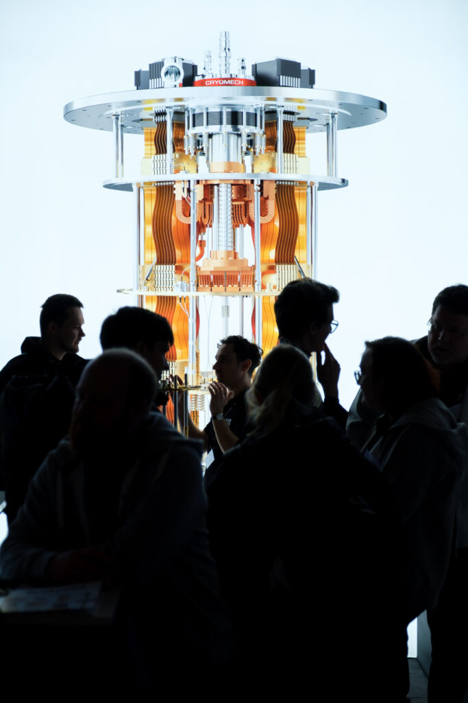 Silhouetten einiger Menschen vor einem großen, leuchtenden Banner mit einem abgebildeten High-Tech-Gerät