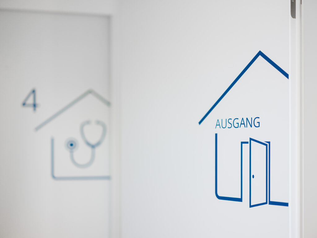 Wandsymbol mit Haus- und Stethoskopsymbol in einer Arztpraxis, aufgenommen von Architekturfotograf Alexander Gerner.