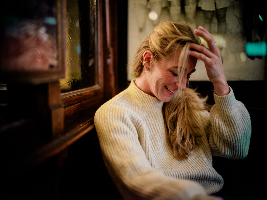 Emotionales Portrait im Orphée Regensburg: Frau im hellen Pullover berührt ihre Stirn und streicht ihre Haare nach hinten – Portraitfotografie von Alexander Gerner.