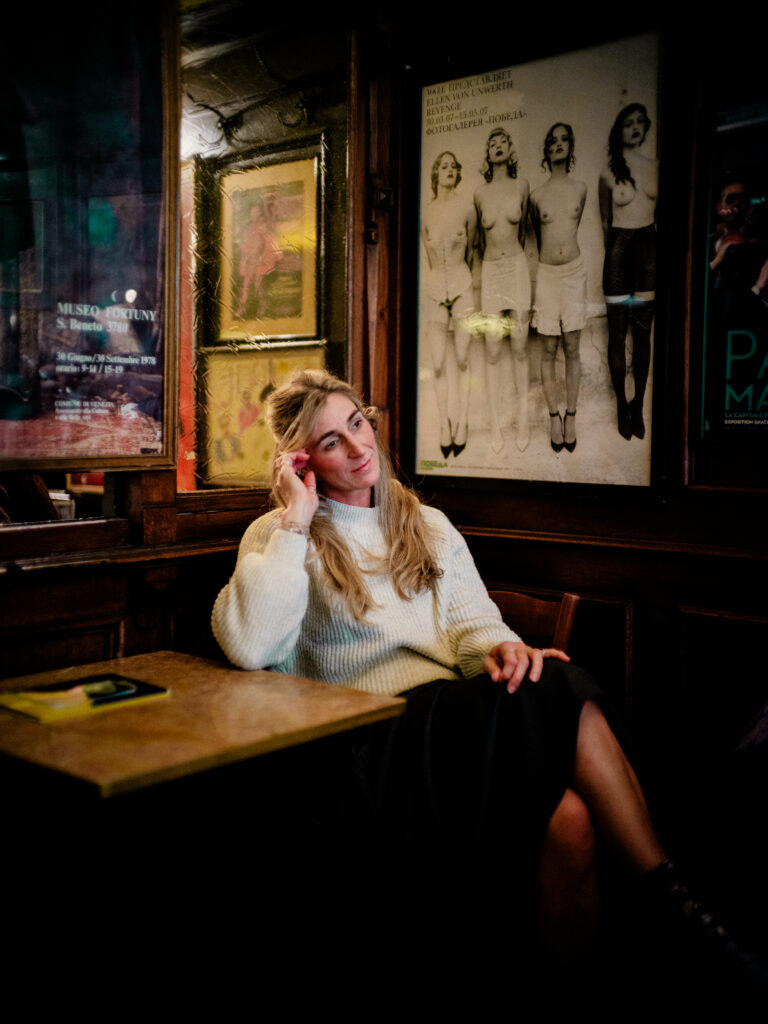 Emotionales Portrait im Orphée Regensburg: Frau im hellen Pullover schaut nach rechts aus dem Bild, im Hintergunrd Wandbilder und Details – Portraitfotografie von Alexander Gerner.