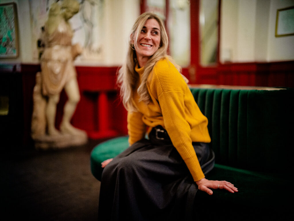 Editorial- und Portraitfotografie Regensburg: Frau mit gelbem, legerem Pullover sitzt entspannt auf rundem, grünem Sitzmöbel im Orphée, fotografiert von Alexander Gerner.