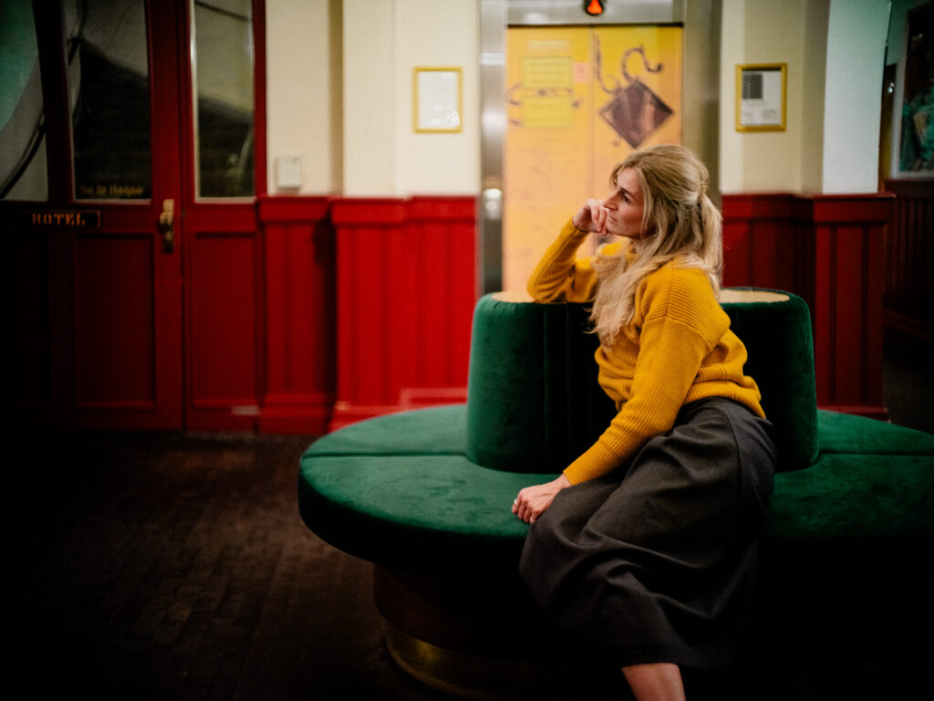 Authentische Portraitfotografie von Alexander Gerner: Frau in gelbem Pullover sitzt auf rundem Sofa im Orphée Regensburg.