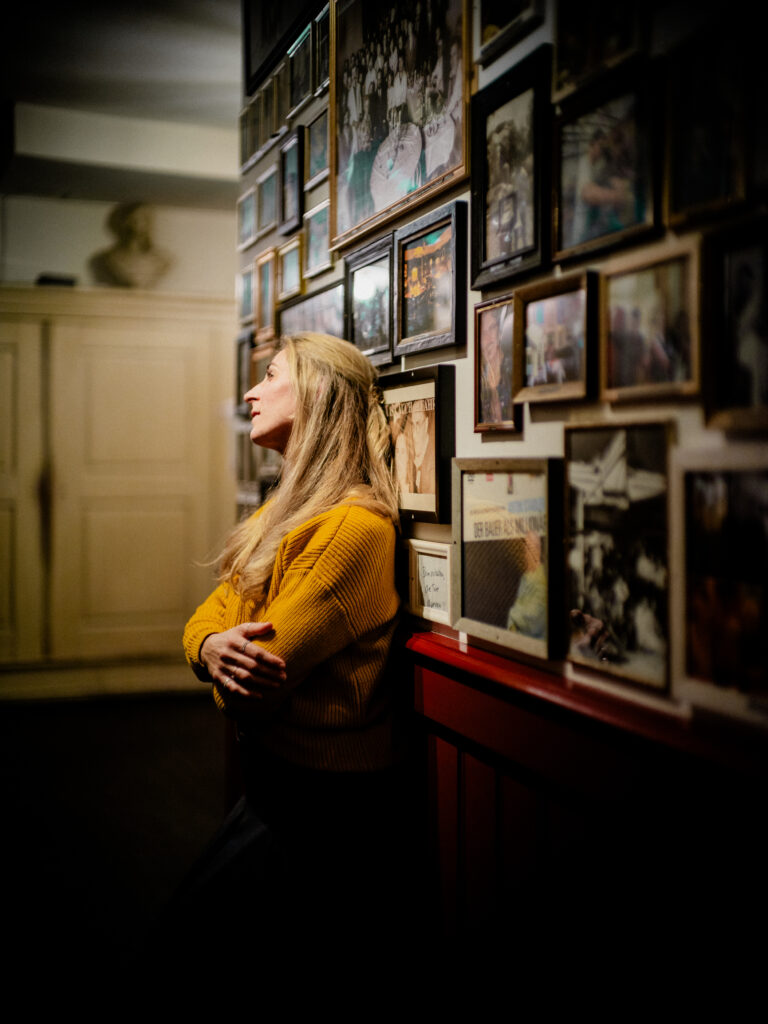 Portraitfotografie Regensburg von Alexander Gerner: Frau lehnt seitlich vor einer Galerie aus eingerahmten Fotografien im Restaurant Orphée.