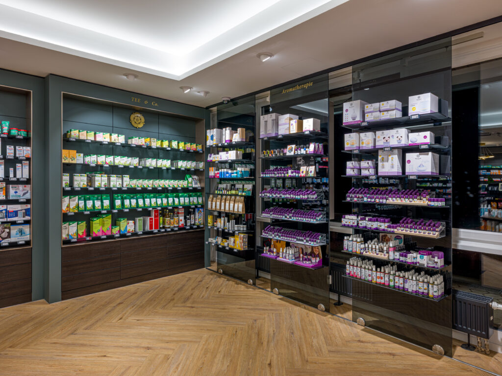Innenraum mit beleuchteten Produktregalen und verschiebbaren Glaswänden mit Produkten am Fenster – Architekturfotograf Alexander Gerner dokumentiert die Rosenapotheke Rosenheim