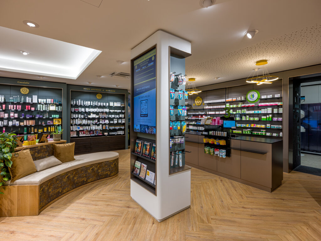 Weitwinkelaufnahme des Verkaufsraums mit Sitzbereich und zentraler Säule mit Informationsbildschirm, Verkaufsbereich und Informationsmaterial – Architekturfotograf Alexander Gerner Rosenheim