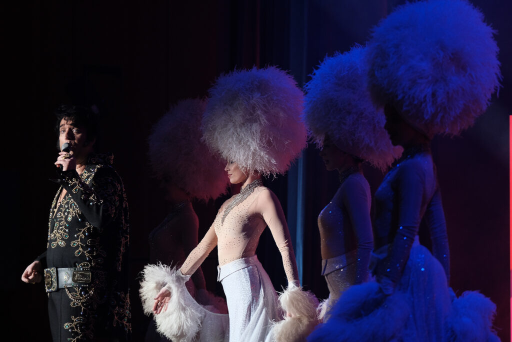 Elvis-Show eines Künstlers auf der Bühne am Mikrofon mit Tänzerinnen im Spotlight, Konferenzfotograf Stuttgart musikalische Performance #nxtKNOWLEDGE 2025.