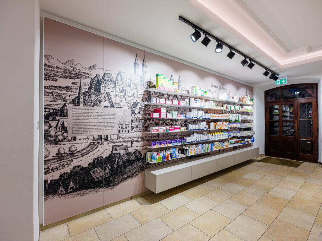 Verkaufsraum mit Wandgrafik und beleuchtetem HV-Tresen – Interior Design von Planquelle