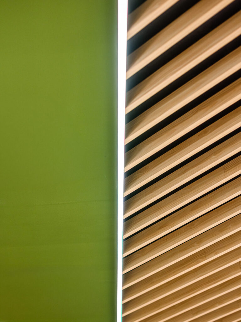 Abstraktes Detail von Holzlamellen vor grüner Decke, Spiel mit Schatten und Licht.