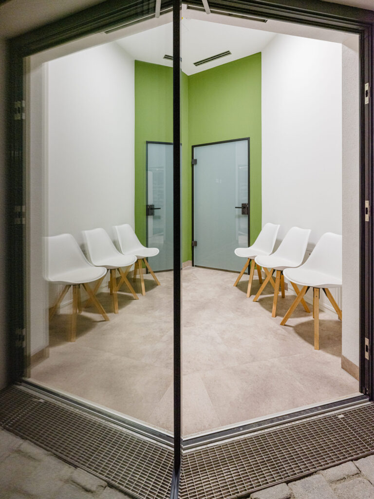 Außenansicht/Eingangsbereich mit Blick durch die Glasfassade in die beleuchtete Apotheke.