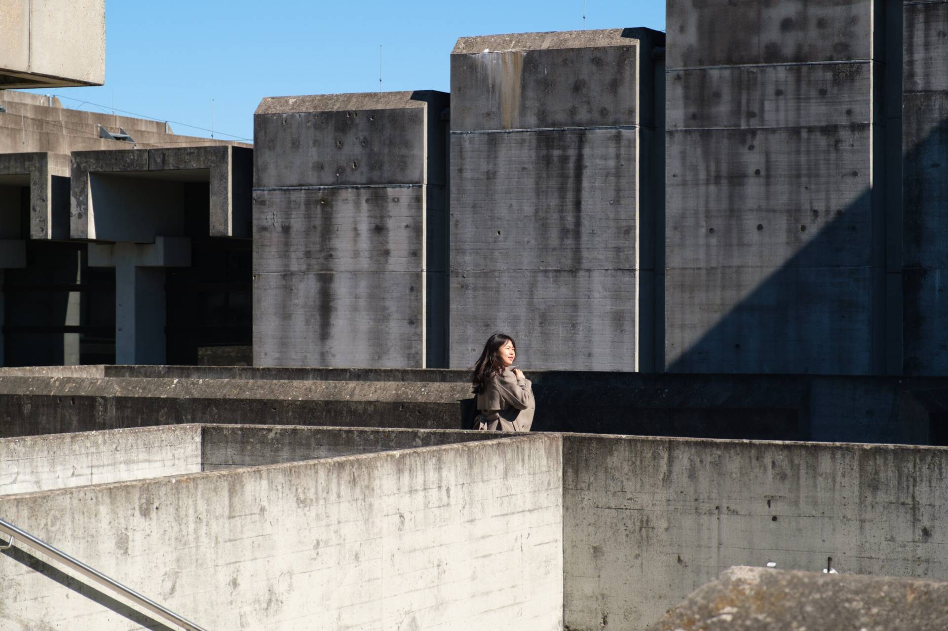 Eine Besucherin asiatischen Aussehens in der Umgebung der nackten Betonarchitektur der Universität Regensburg